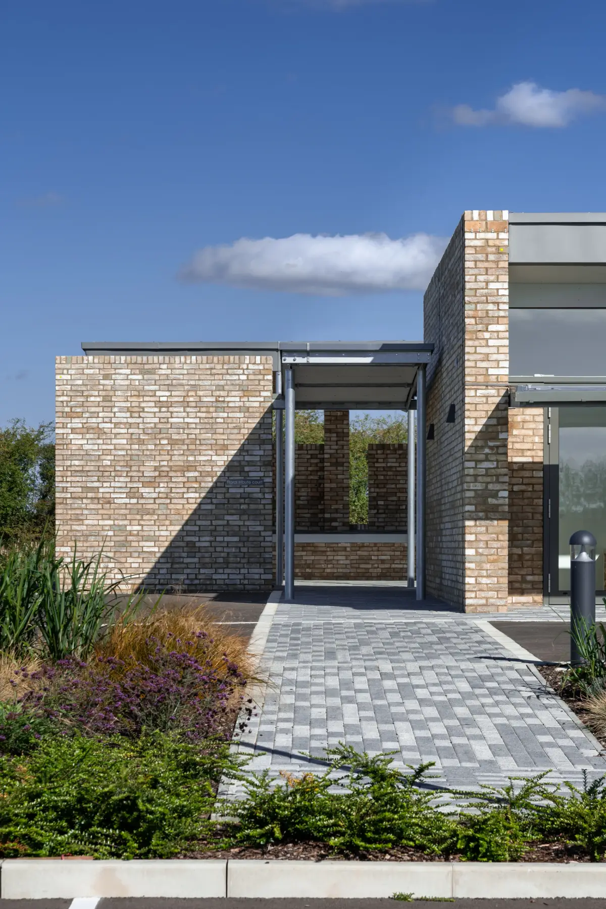 A brick entrance court in full sun, a covered walkway framing a view through to planting beyond