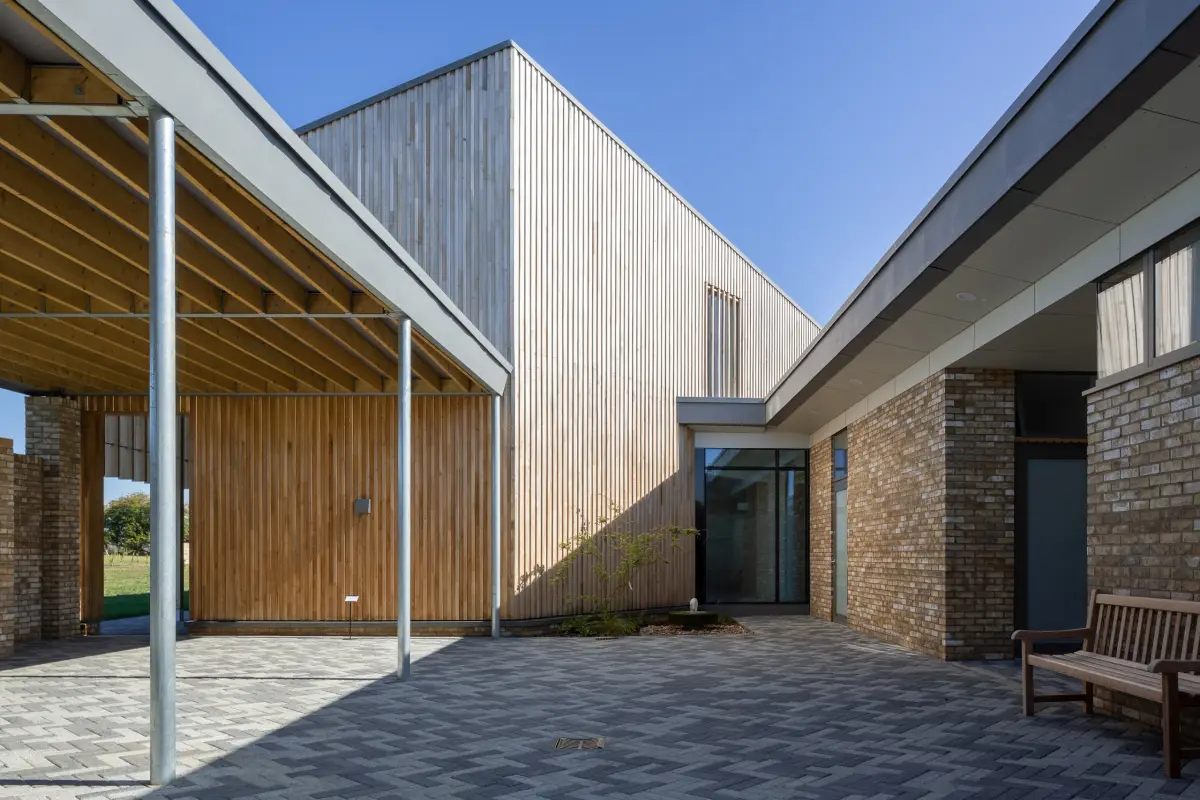 A courtyard between wings, pale vertical timber cladding above brick, the paved floor running to a glazed link
