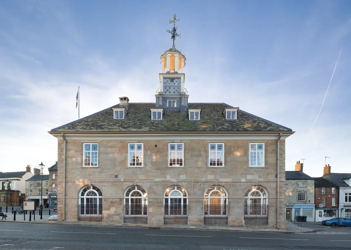 The town hall from the market place at dusk, its arcaded ground floor lit and the weathervane above the cupola